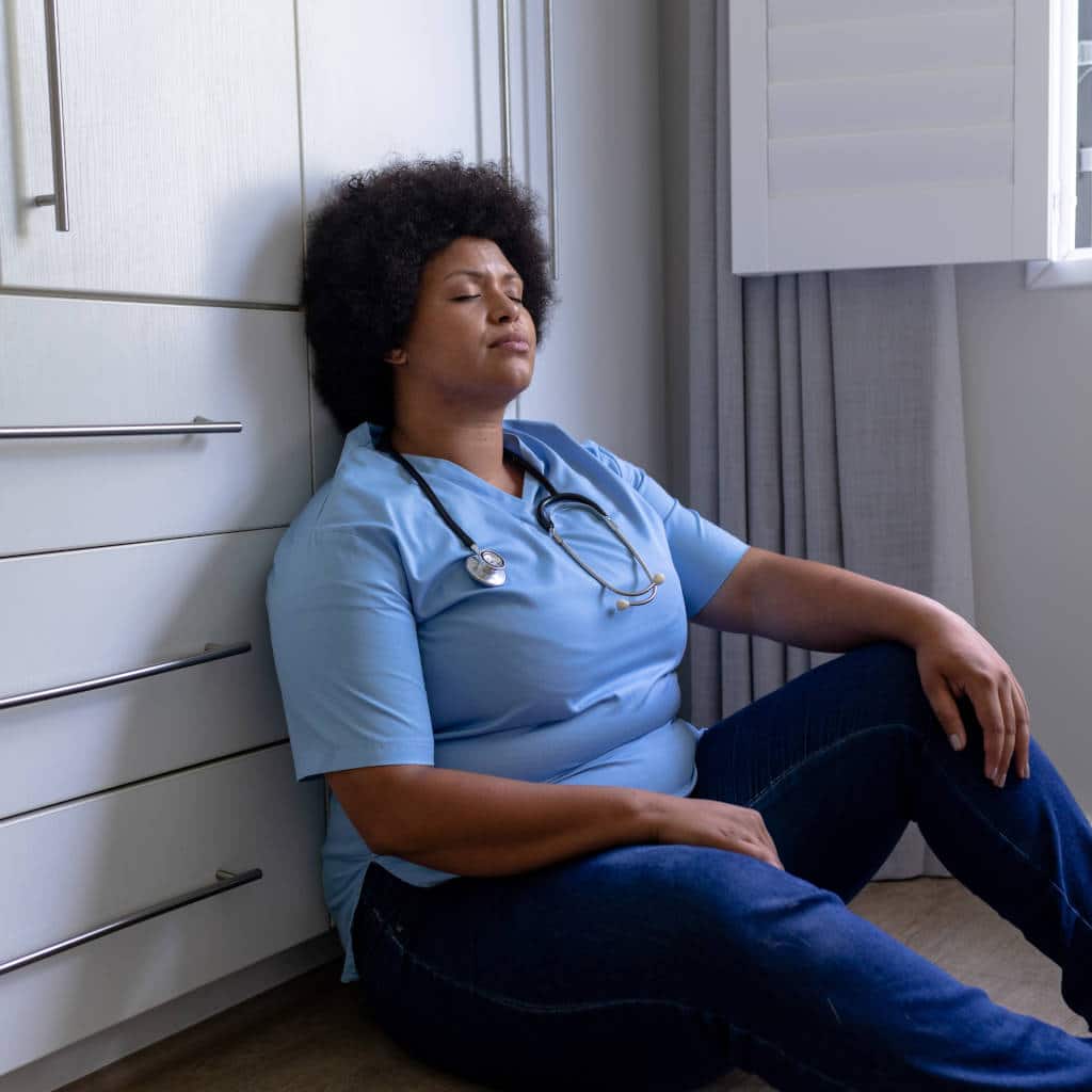 african american nurse sitting on floor in hospital