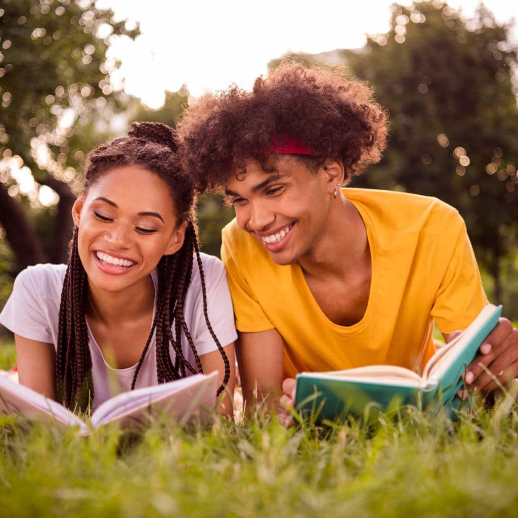 young couple laying on grass in park reading book